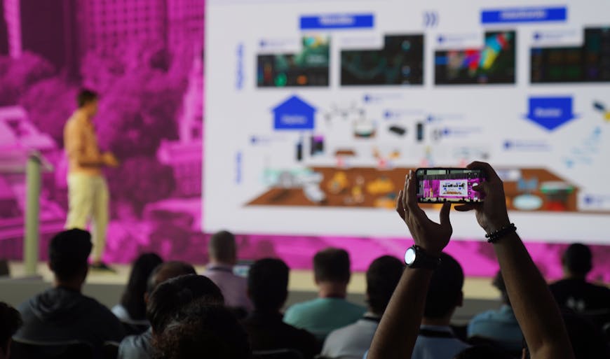 An attendee of the 2025 Cesium Developer Conference in Philadelphia takes a photo with their phone of a presenter session.