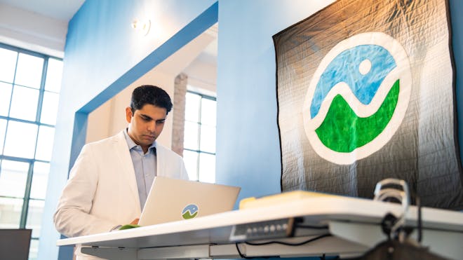 A man in a white blazer uses a laptop at a standing desk next to a Cesium quilt.