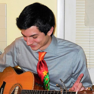 A man in a red tie plays an acoustic guitar.