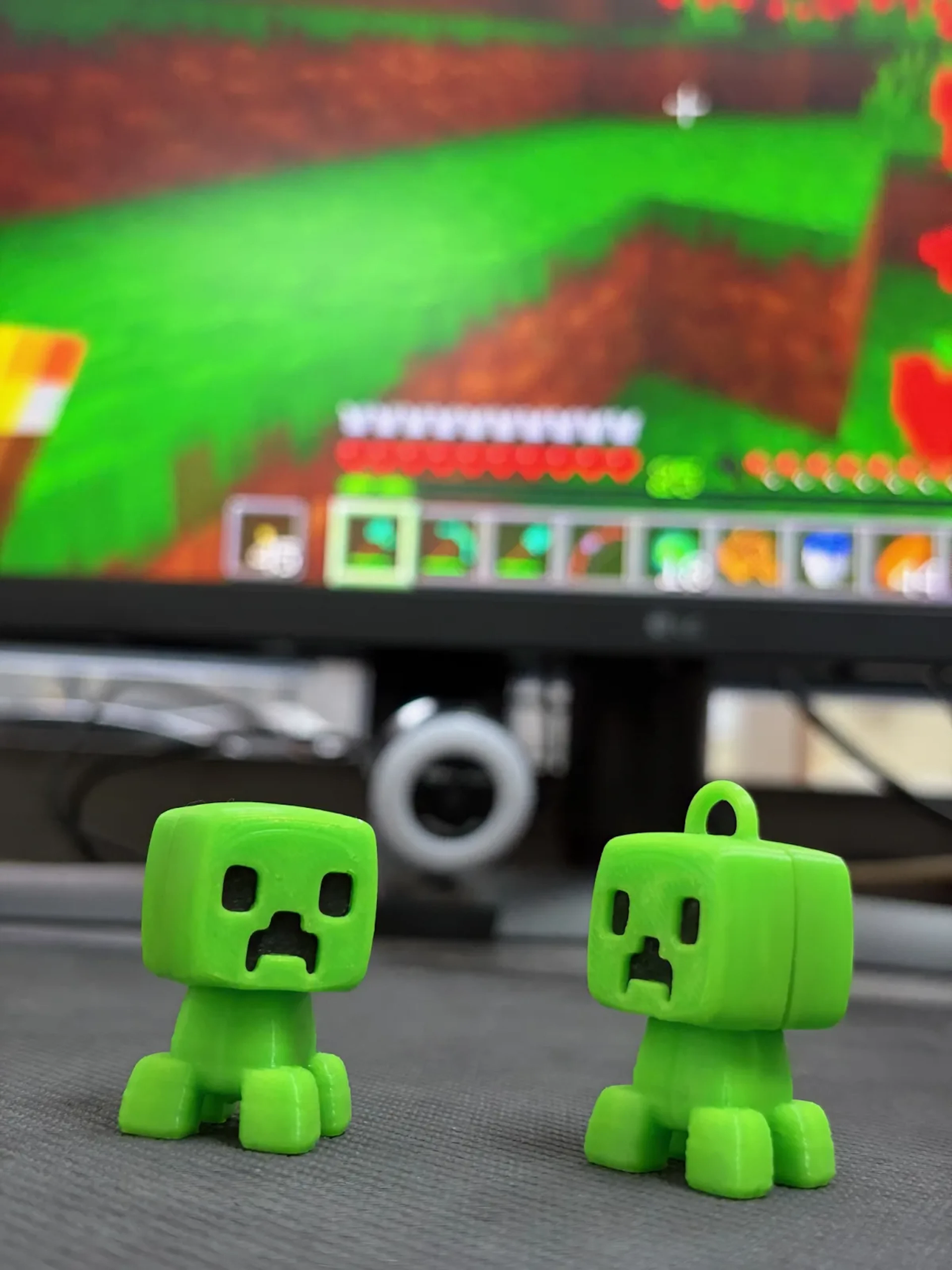 Two green Minecraft creeper figures standing in front of a monitor