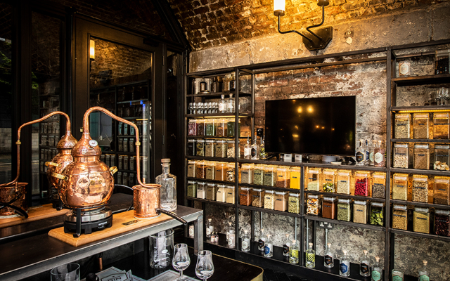 A shelving unit full of jarred botanicals and a small copper still on display
