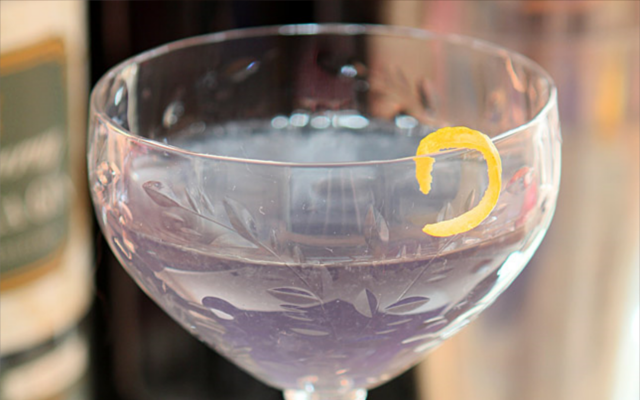 Purple cocktail in martini glass with lemon zest peel
