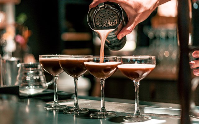 Cocktails being poured through a hawthorne strainer