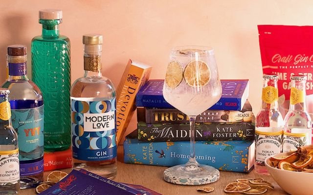 A collection of books, a gin and tonic in a glass and bottles of gin and tonics surrounding