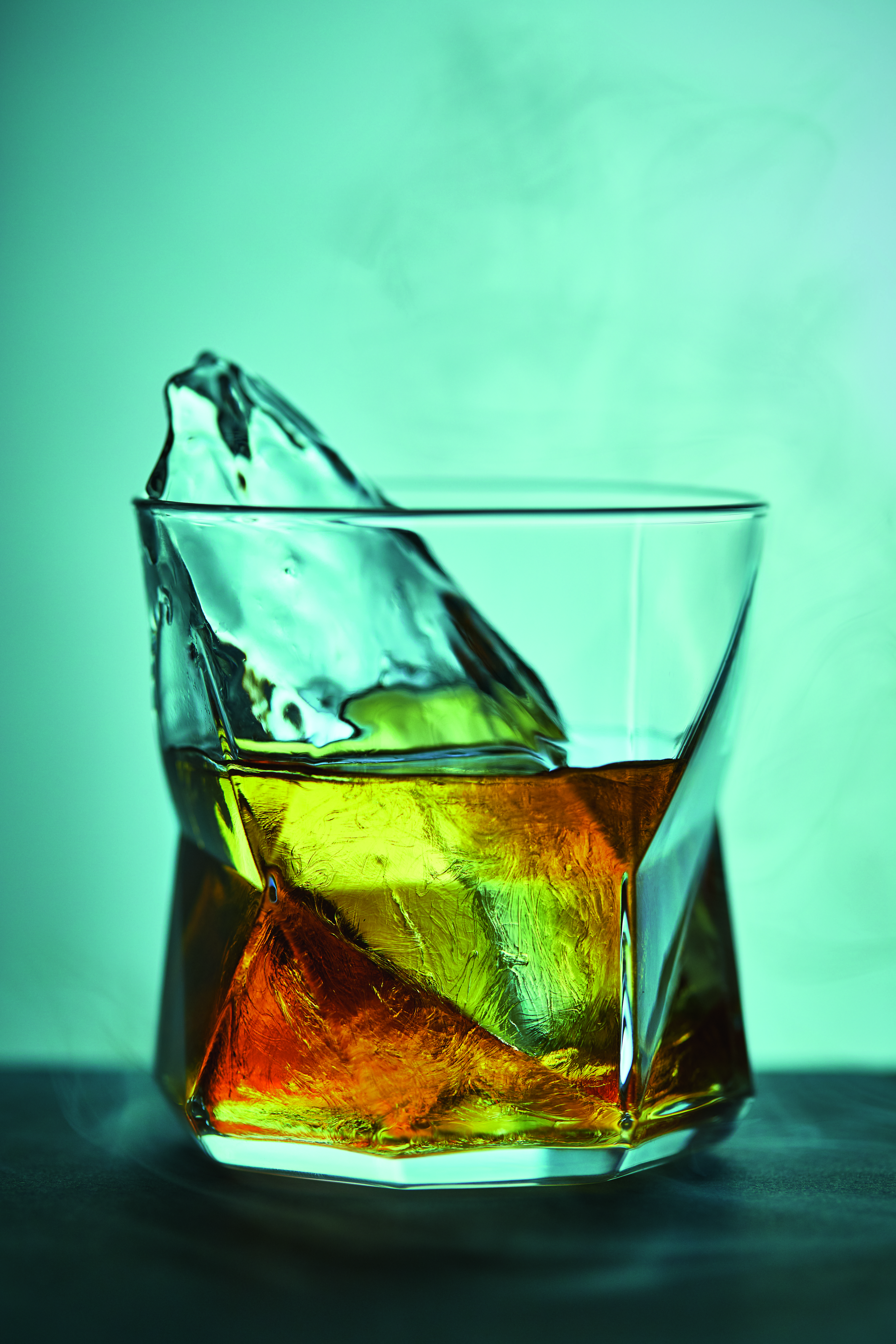 Whisky cocktail in a rocks glass with ice against blue background