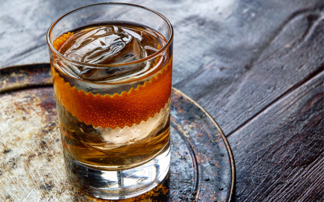 Gin Old Fashioned with orange twist over a block of ice in tumble