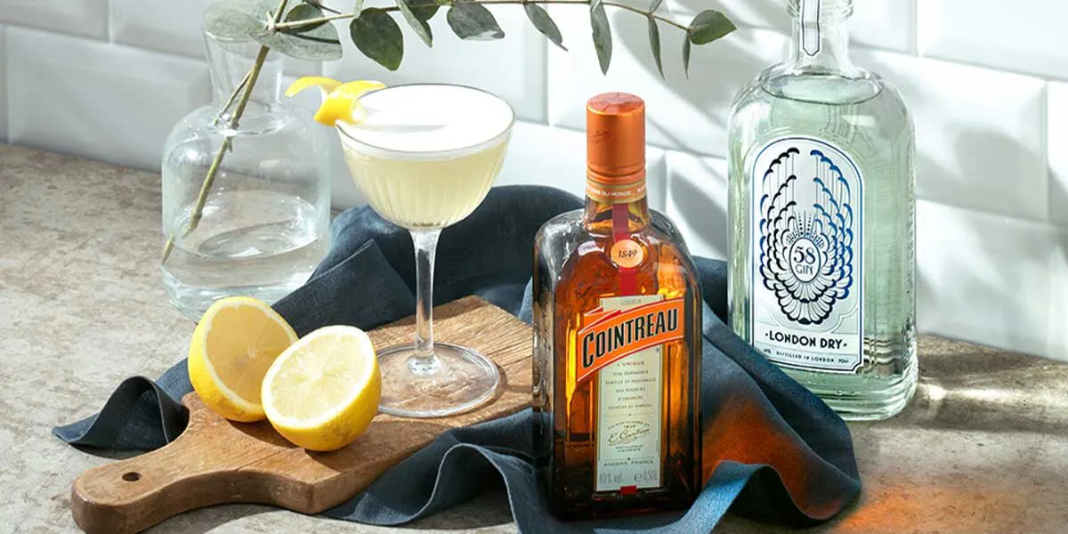 White lady cocktail with bottle of triple sec and gin on board