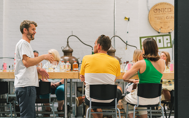 A group of people are sat at wooden tables and learning about gin distillation