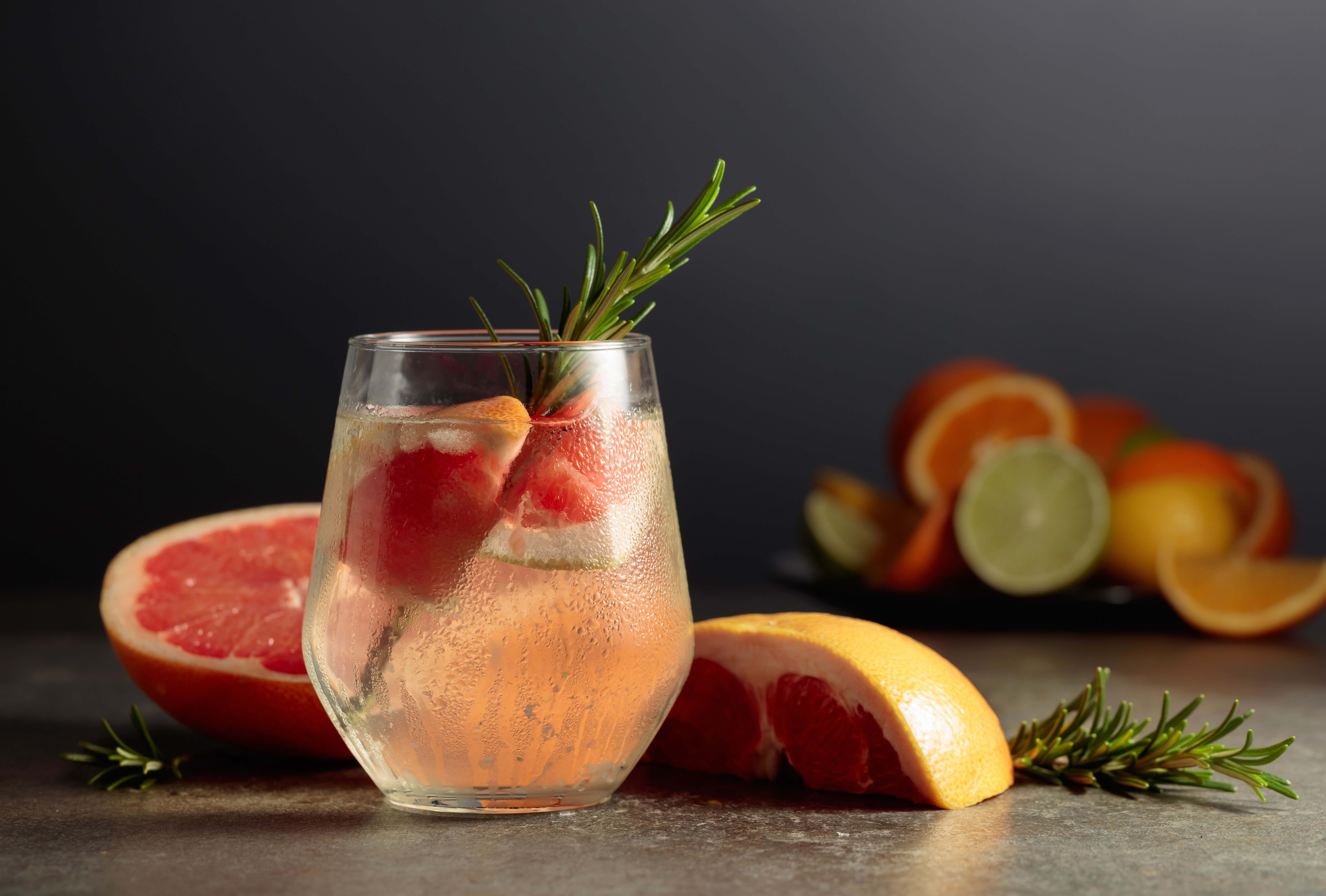 Light pink cocktail in a tumbler garnished with a grapefruit slice and rosemary sprig