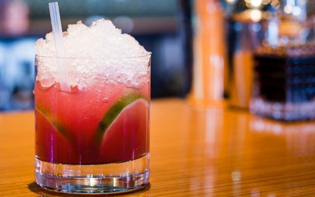 Gin Daisy red cocktail with lime and ice on a bar