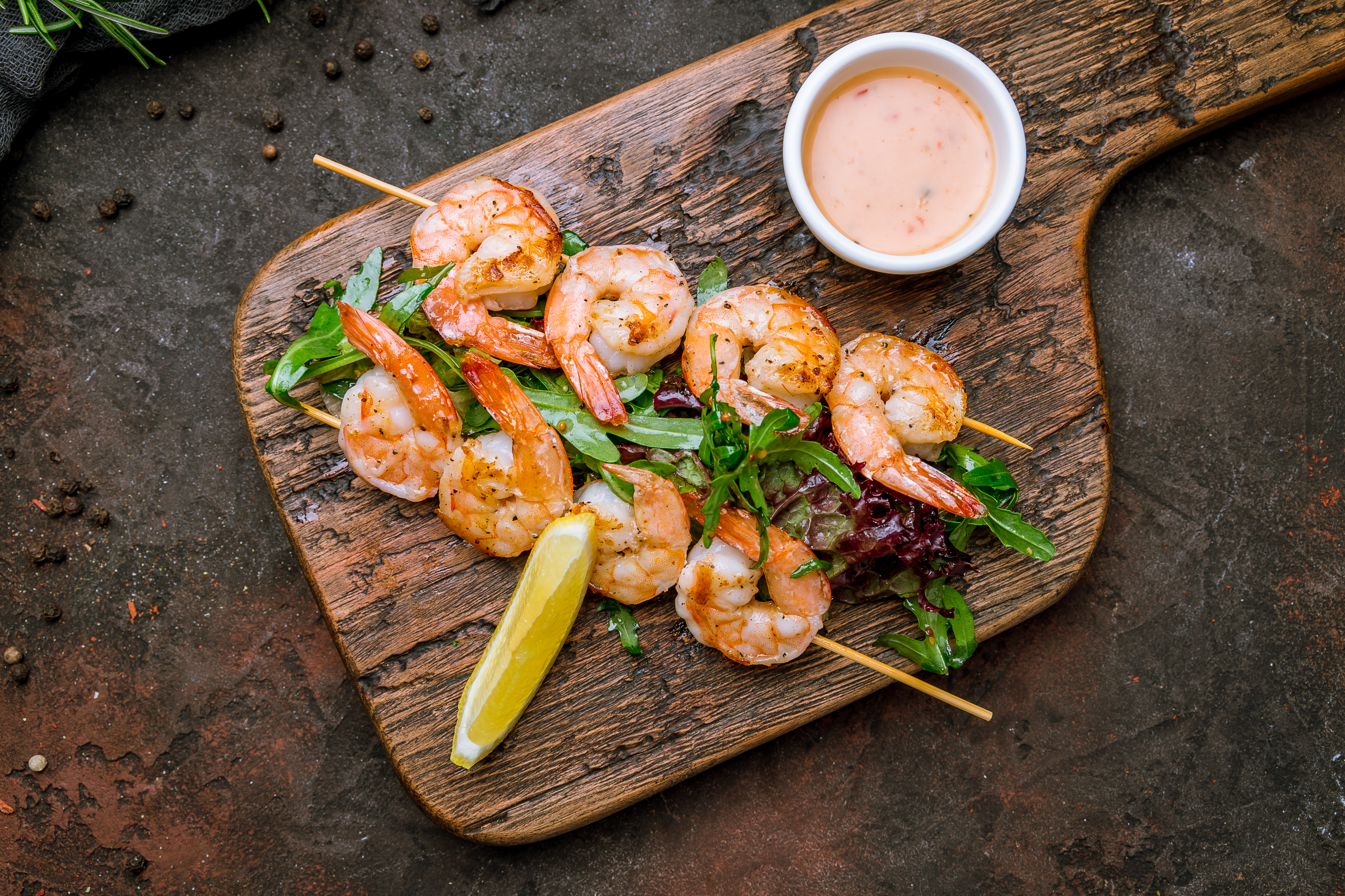 Two skewers of grilled shrimp on a bed of salad with a lemon wedge and dipping sauce
