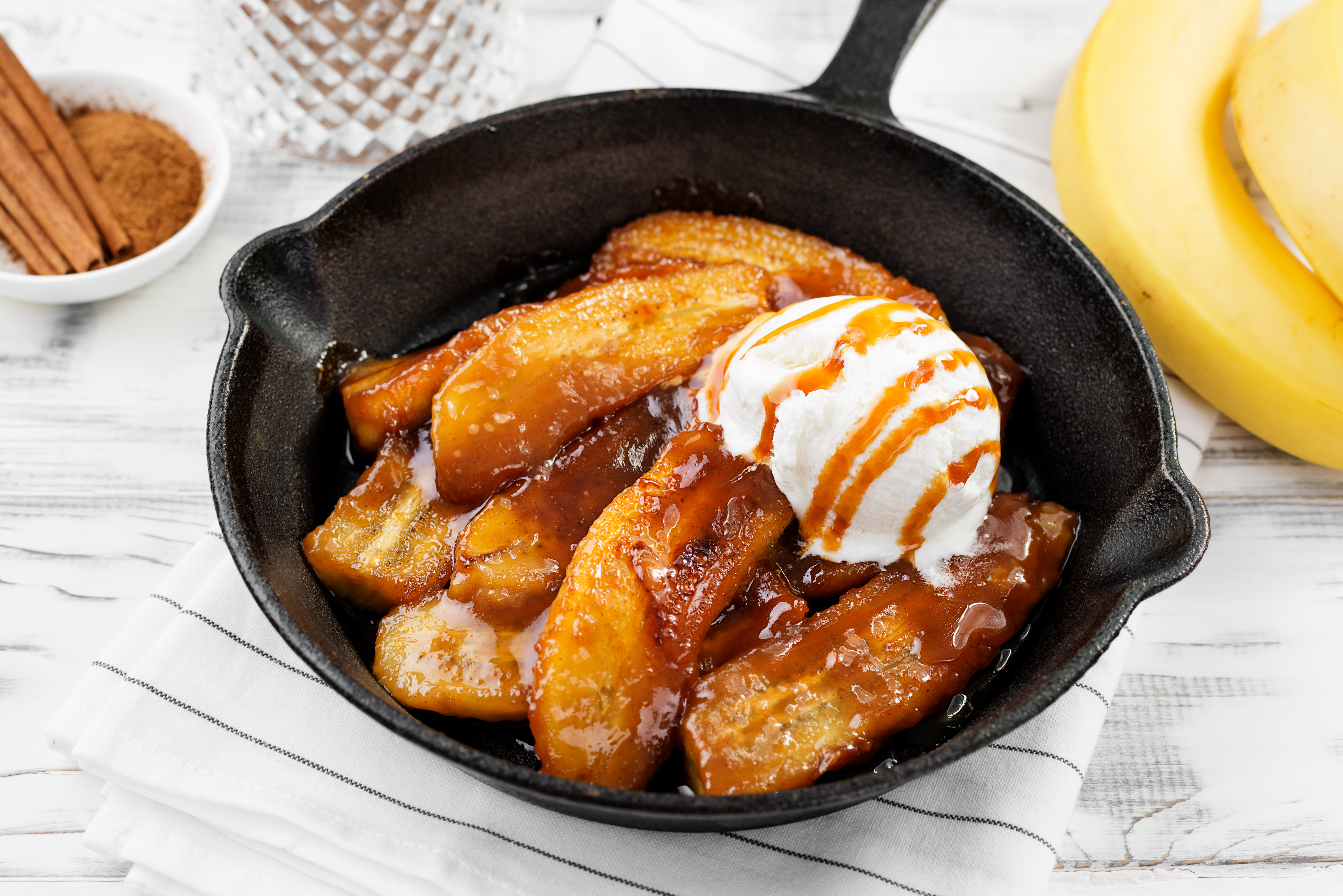 Cooked banana slices topped with a treacle sauce and vanilla ice cream in a black skillet