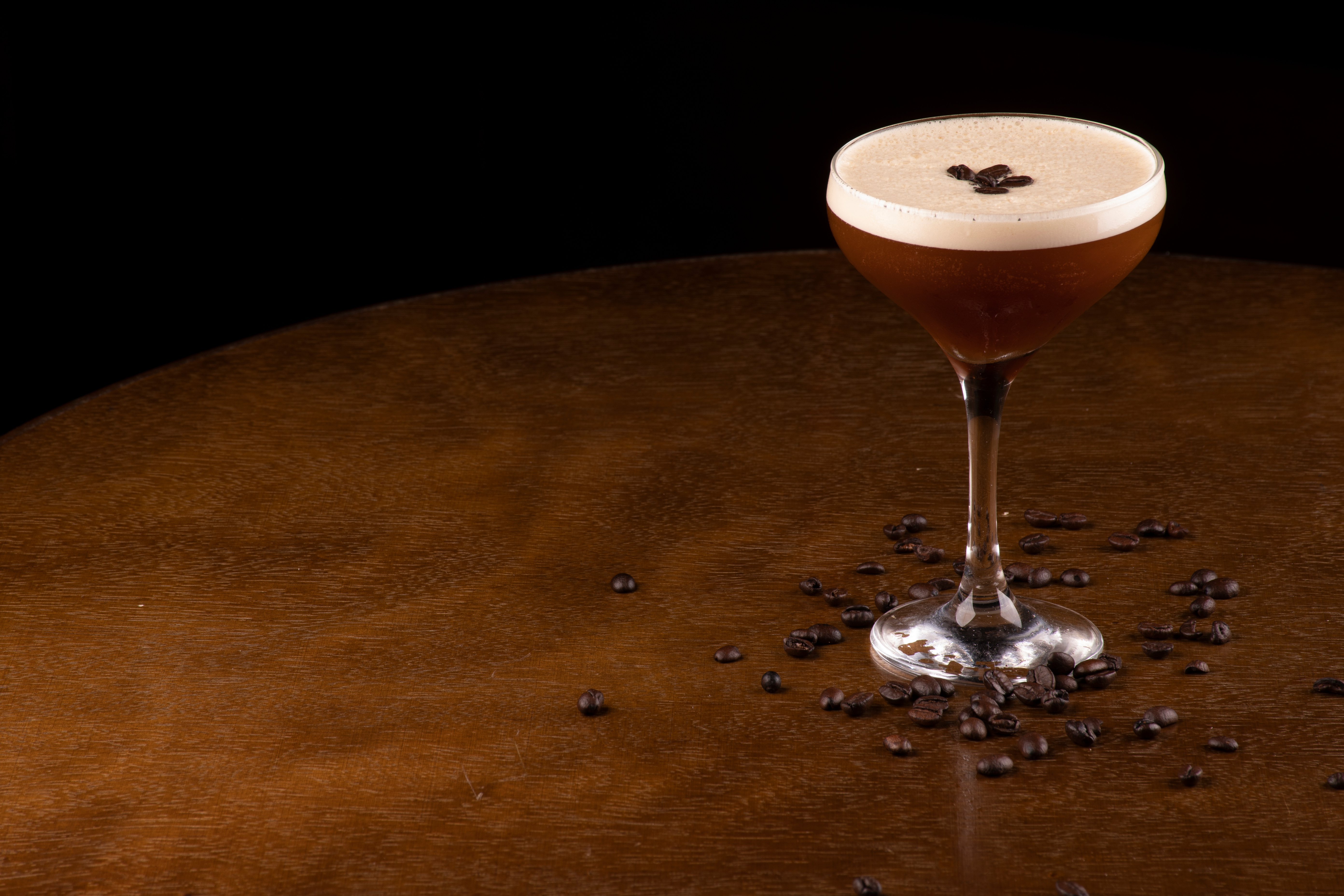 Dark, moody image of an Espresso Martini with coffee beans scattered over the surface that it's stood on
