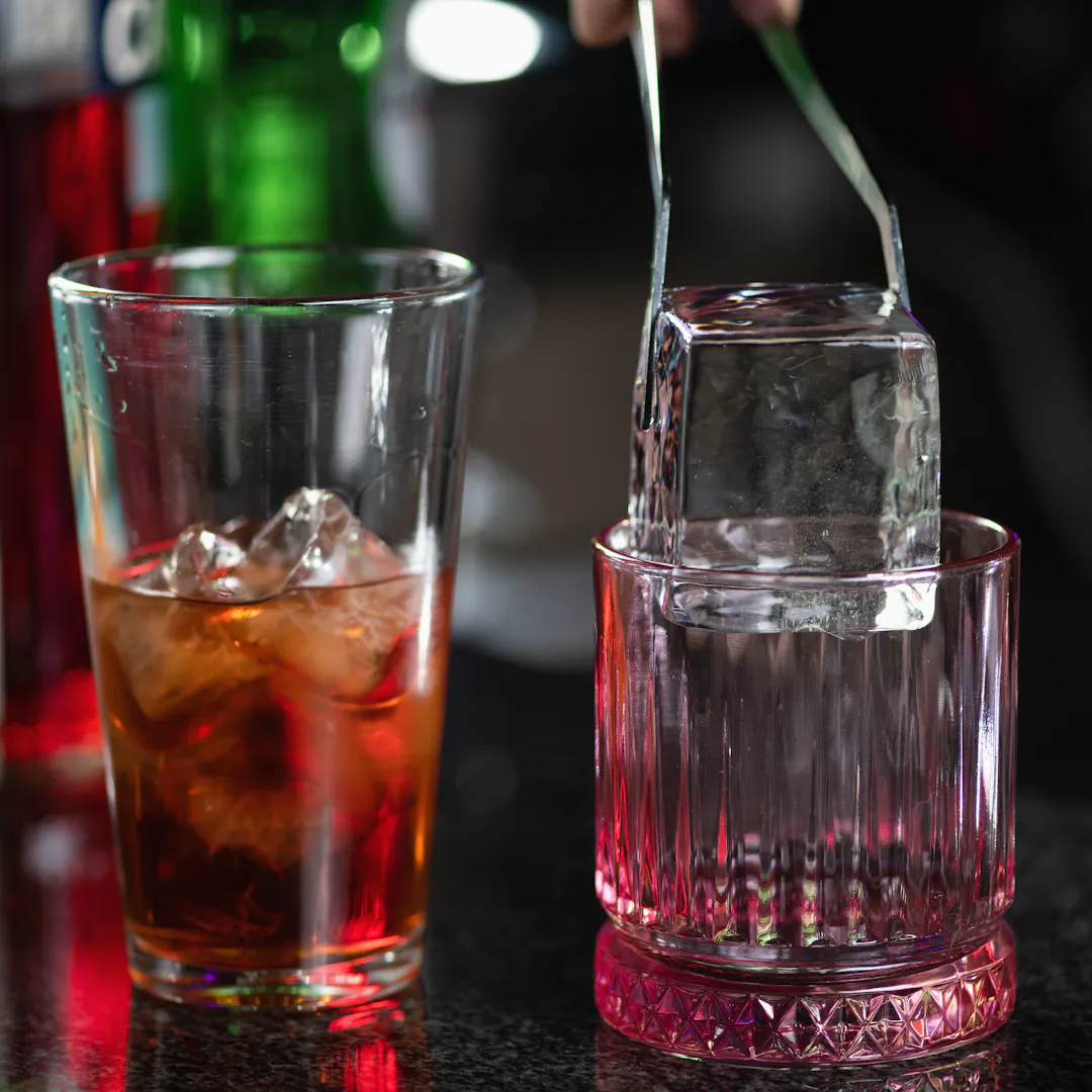 Large square ice cube being placed into a rock glass