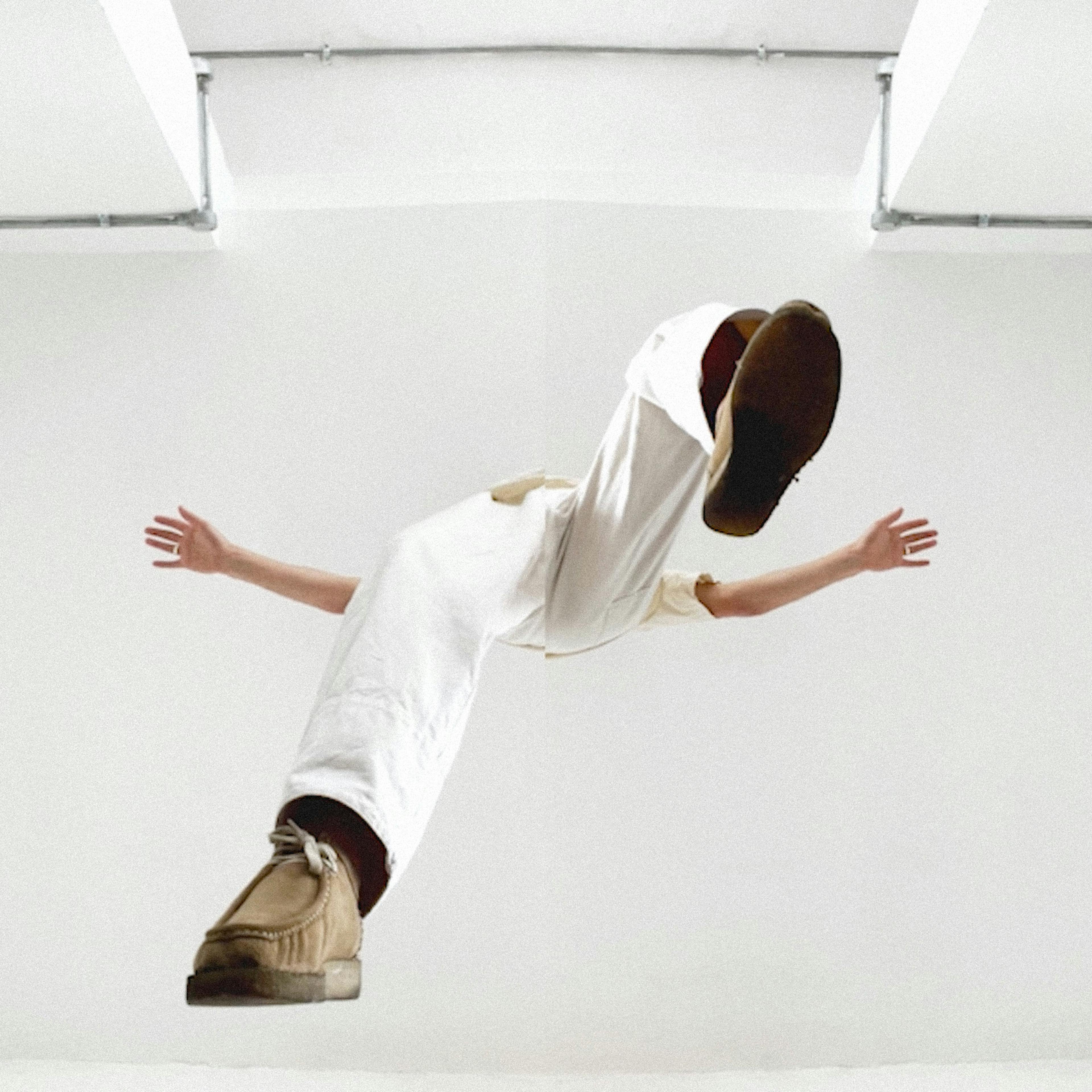 Screenshot from a video of a human figure with white trousers and beige shoes floating in the middle of a white-walled space. 