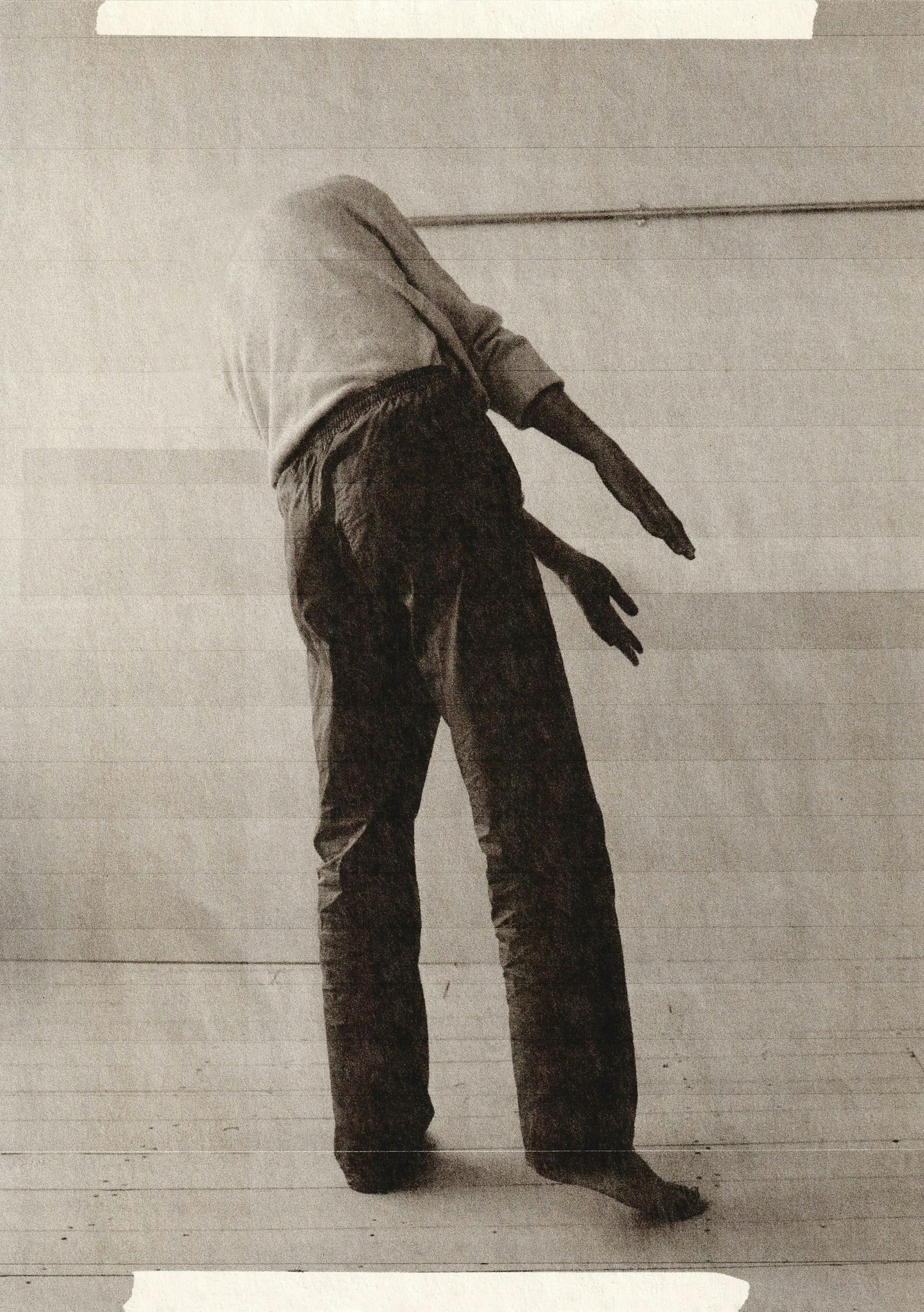 Black and white photograph of a human figure standing up with his back turned towards the camera and his head concealed. 