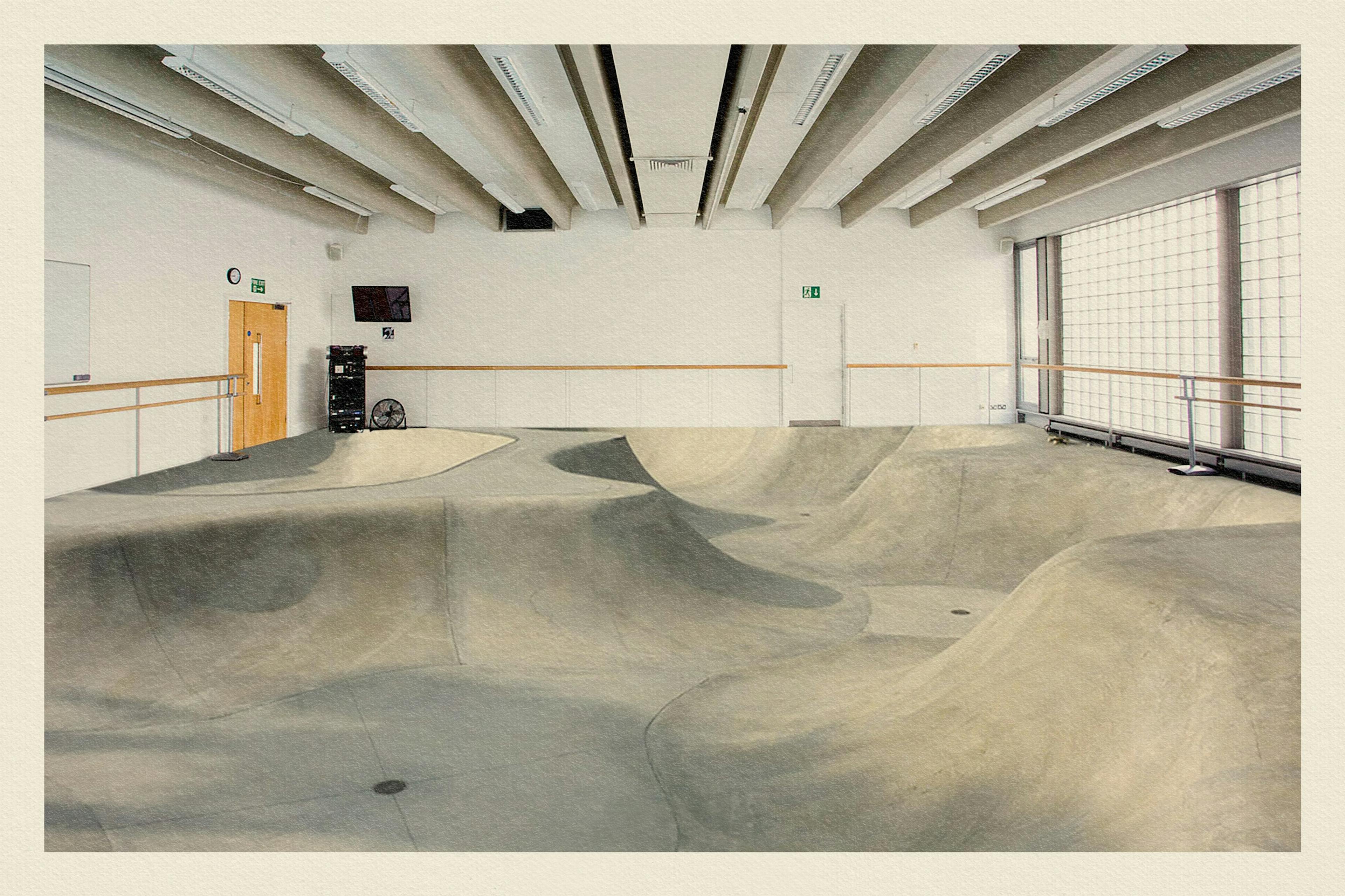 Photograph of a traditional dance studio with ballet bars around the perimeter, which has concrete and ramped flooring.  