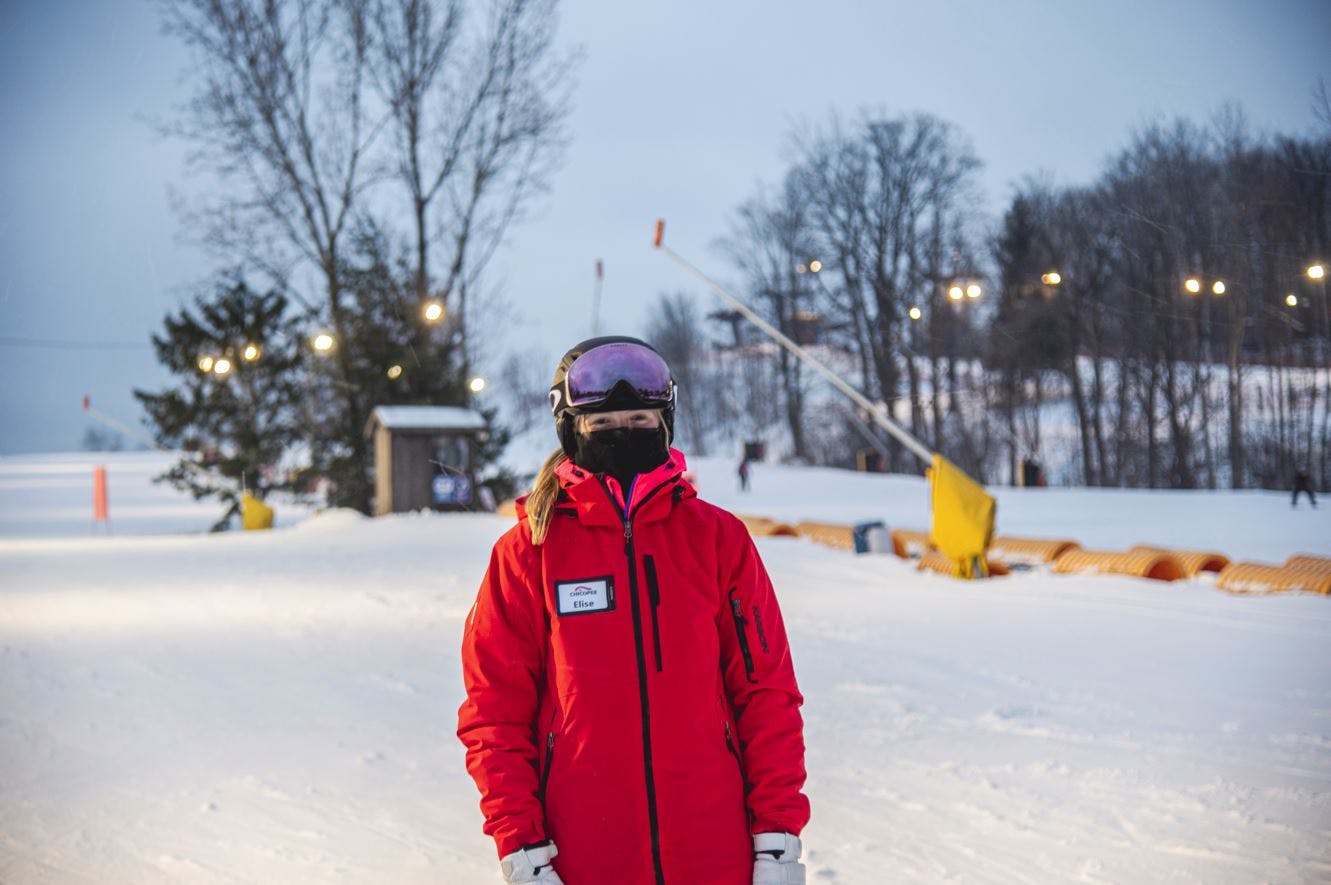 Ski Instructor Elise standing on KidZone in her uniform, her smile is hidden by a face mask. 