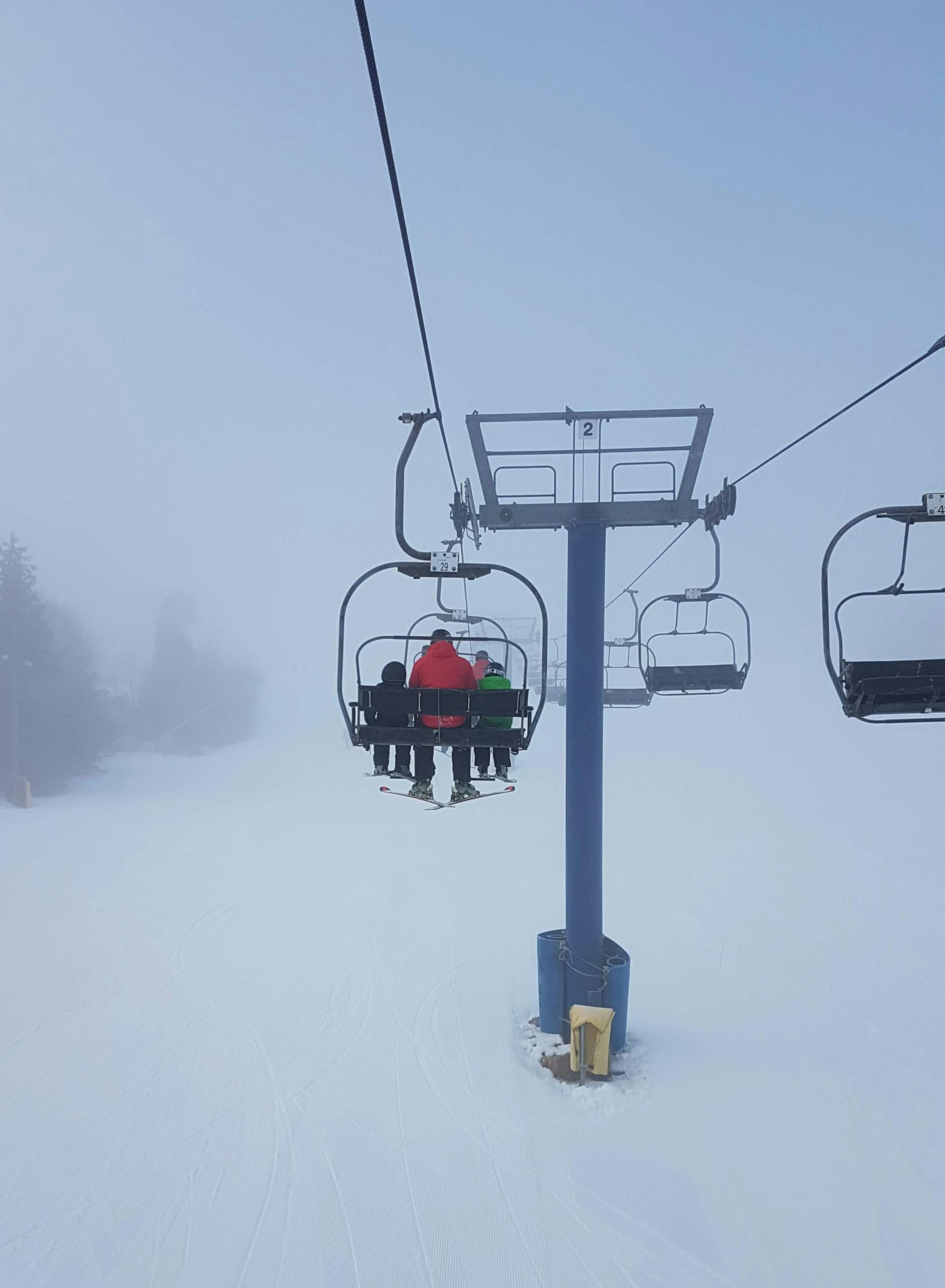 A foggy photo of 3 people on a chairlift, taken from behind. 