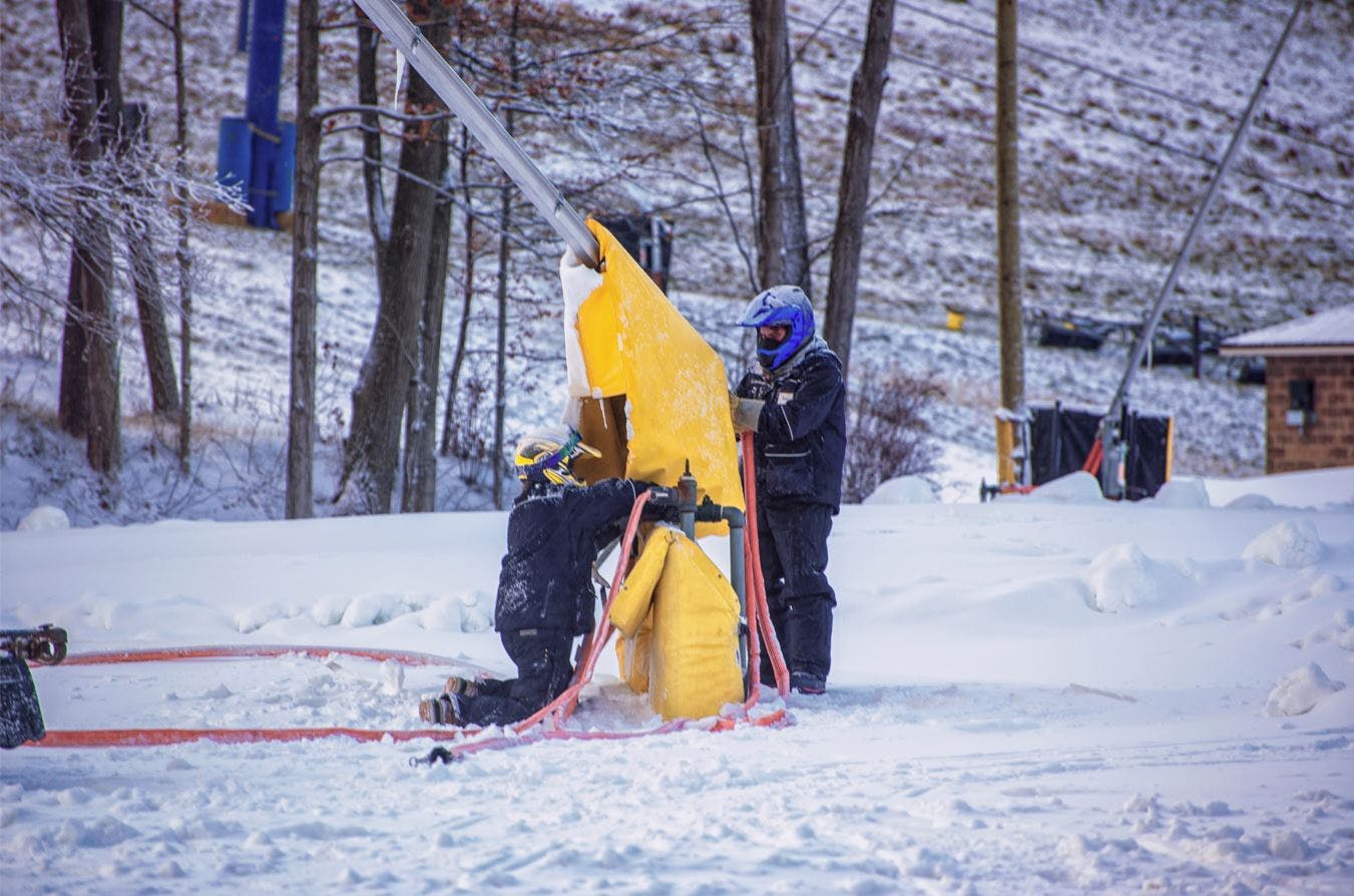Two snowmakers connecting hoses to a snow gun. 