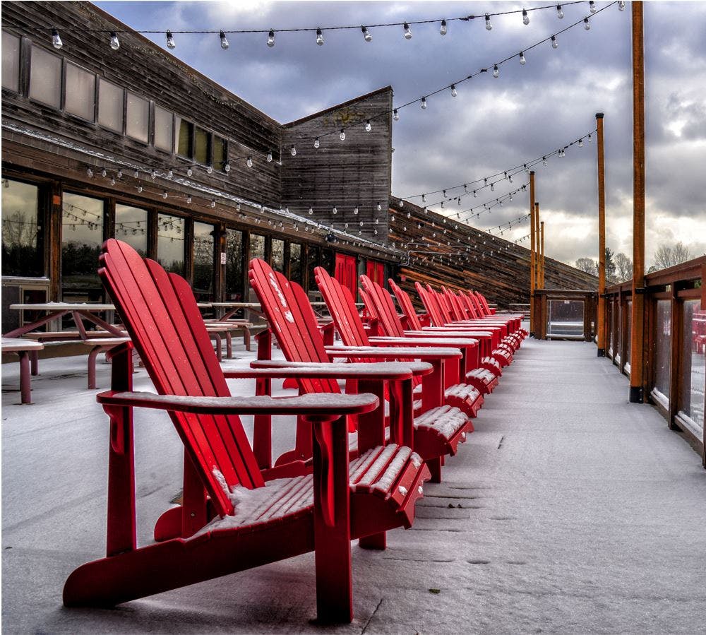 A line of red Adirondack chairs on a snowy deck. 