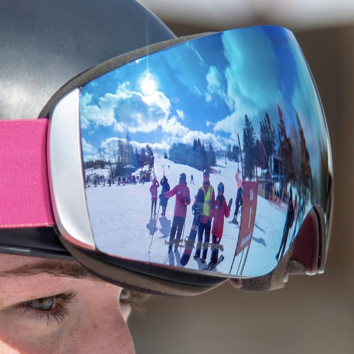 Reflection of happy skiers in a rider's goggles on a bright sunny day