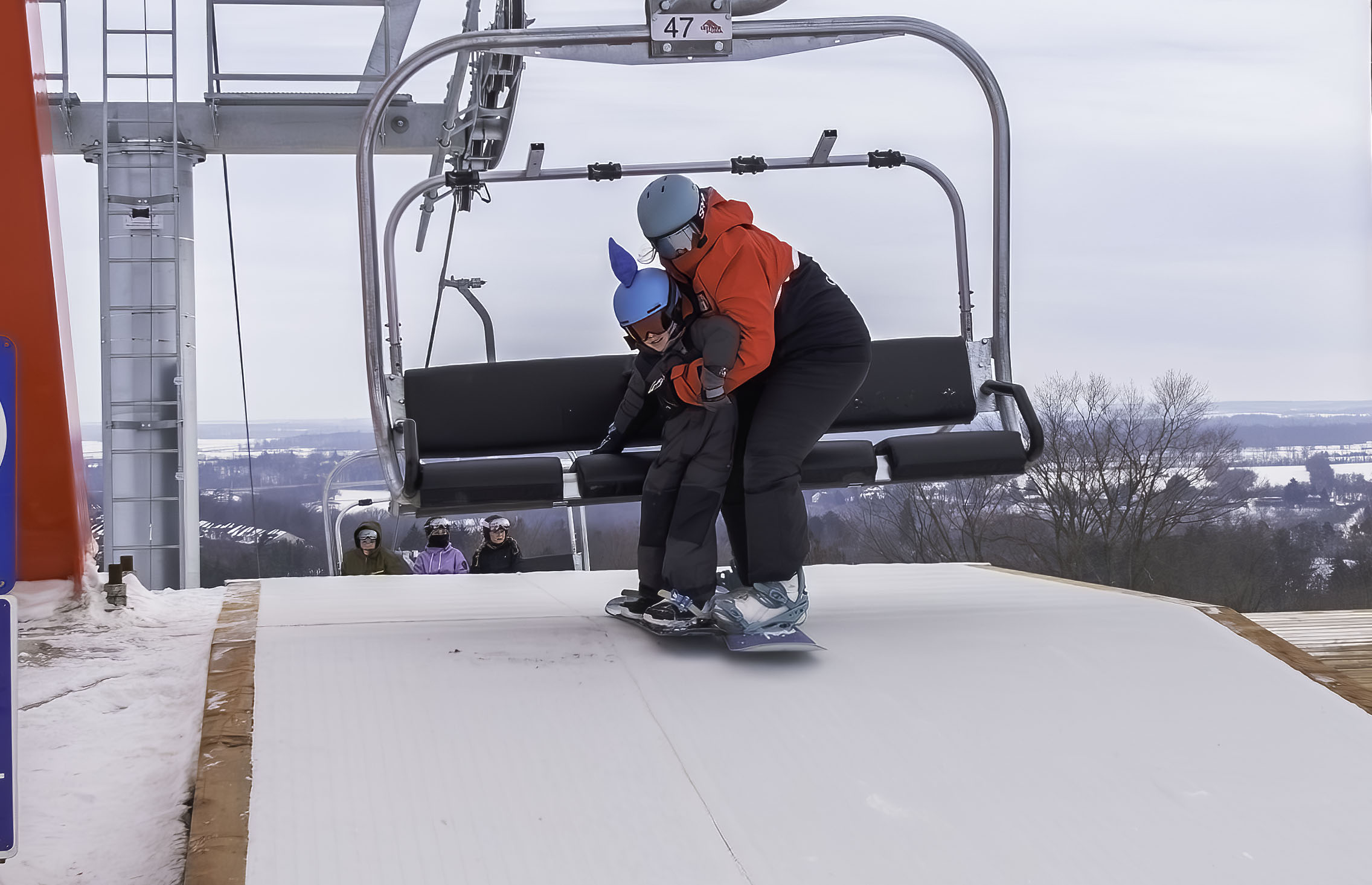Snowboard instructor assisting student off Red Lift.