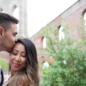 husband kisses his wife on the forehead while they pose in front of a brick building