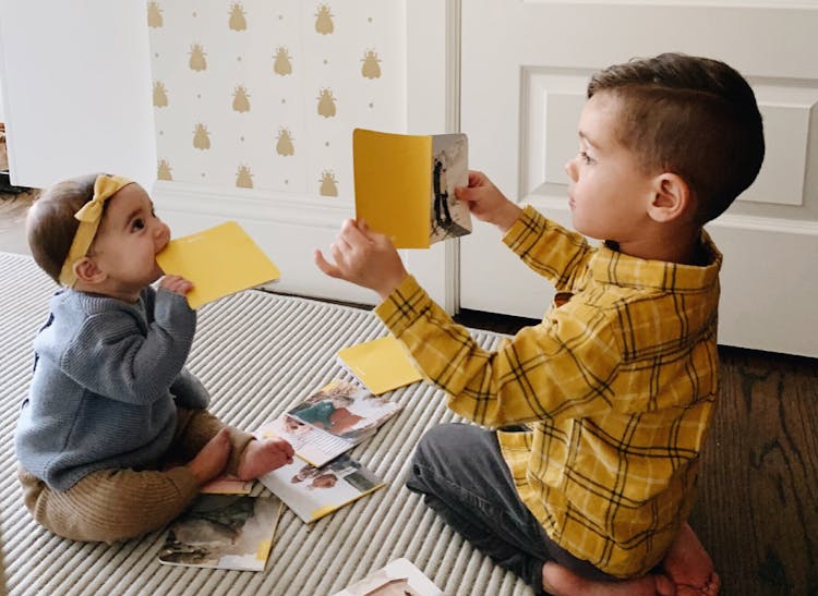 little boy showing monthly photo book to baby sister in nursery
