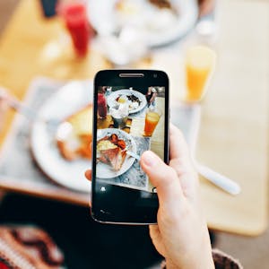 woman holding iPhone over dish taking photo of find with little boy watching