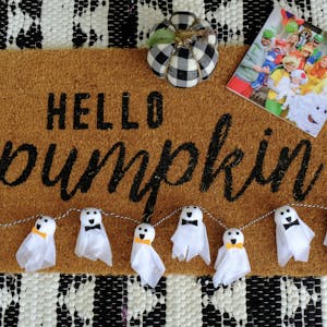 A hello pumpkin doormat with a homemade Halloween garland, pumpkin, and Chatbook on the mat.