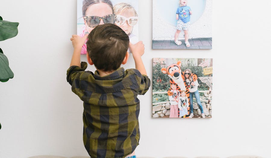A little boy is hanging up family photos while standing on the couch