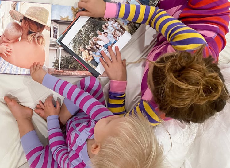 hardcover family photo books open on bed with kids flipping through them