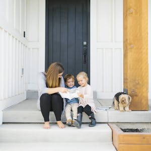 a mom, her 2 kids, and her dog all sit on the porch of their house and look through Chatbooks together.