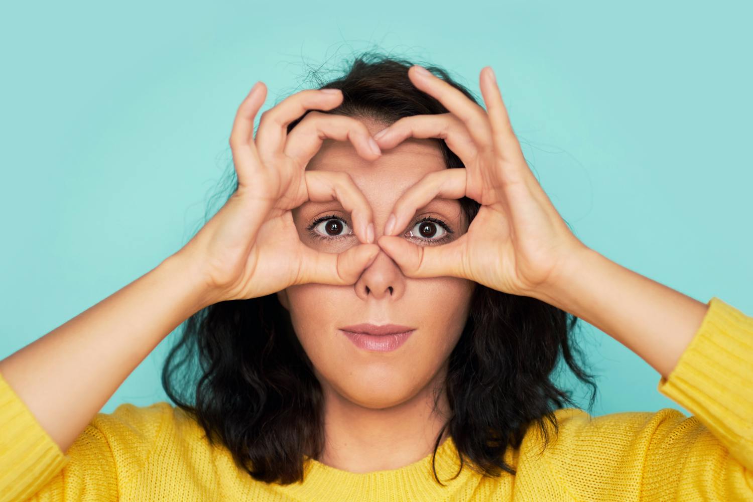 Femme qui forme des lunettes avec ses mains autour de ses yeux.