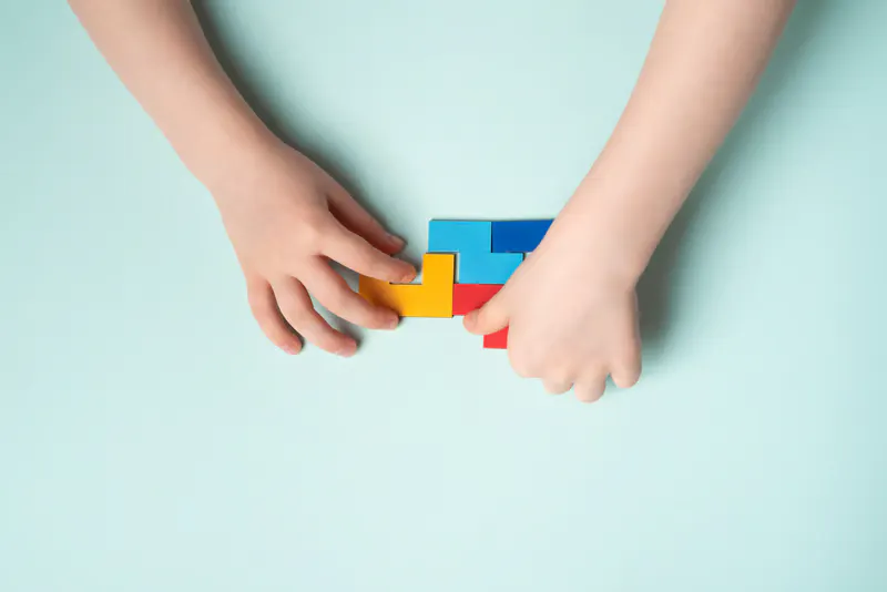 Deux mains d'enfant jouant avec des briques colorées.