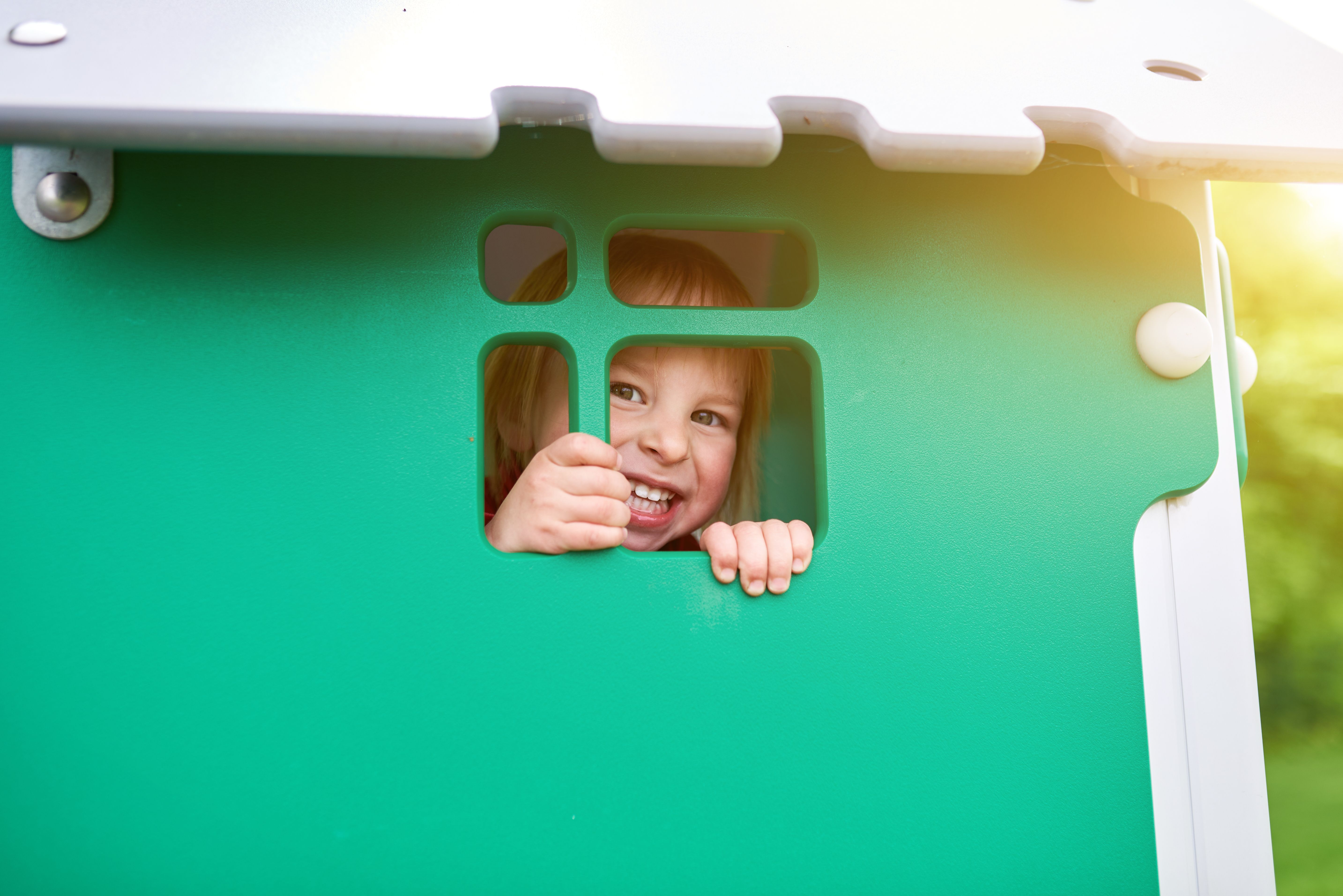 Enfant jouant dans une maison de jardin en plastique verte.