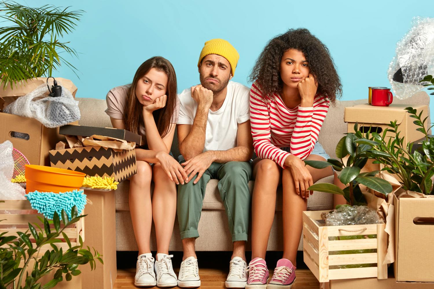 Trois jeunes personnes assises sur un canapé autour de cartons de démenagement.