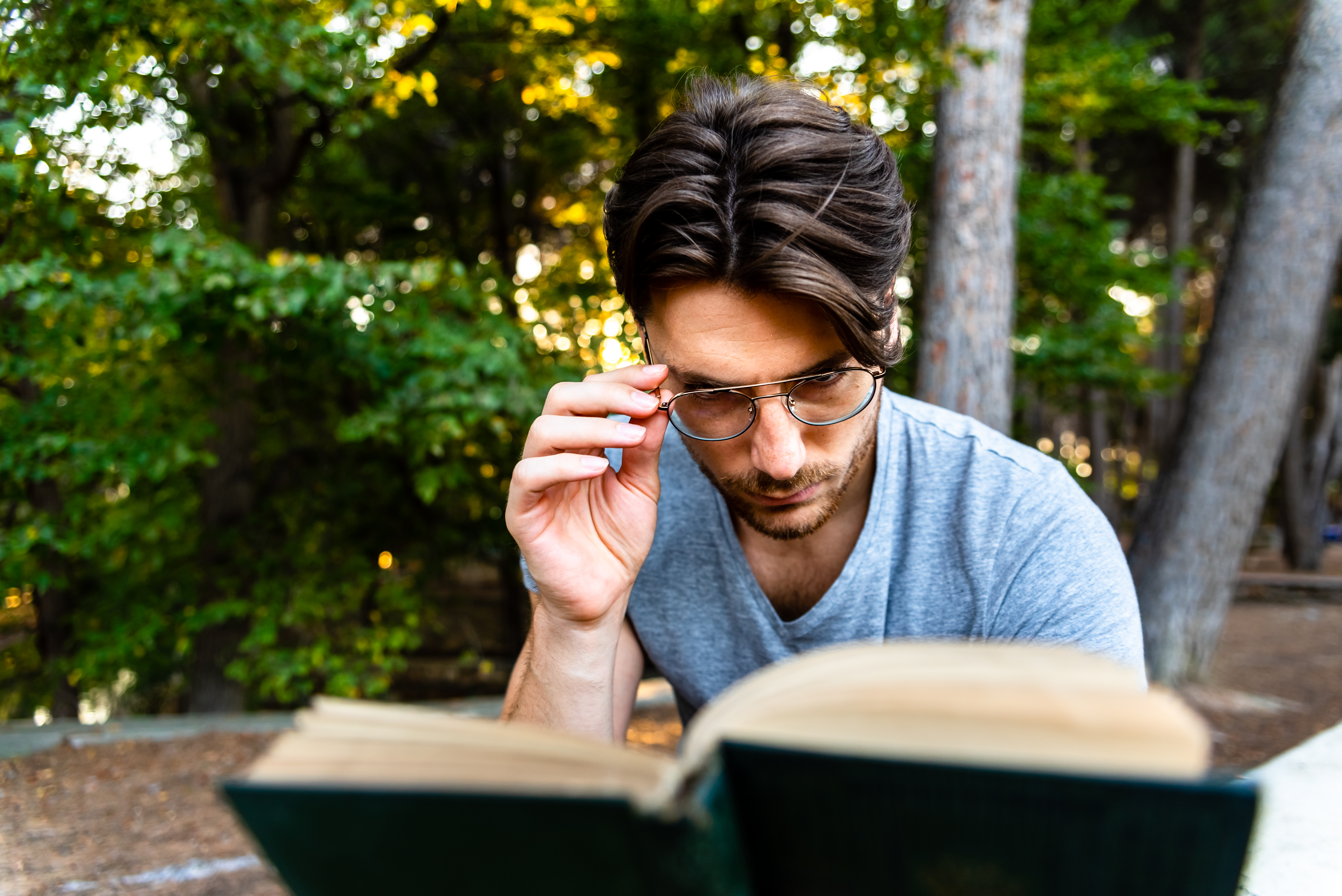Homme tenant ses lunettes sur son nez en train de lire dans un parc.