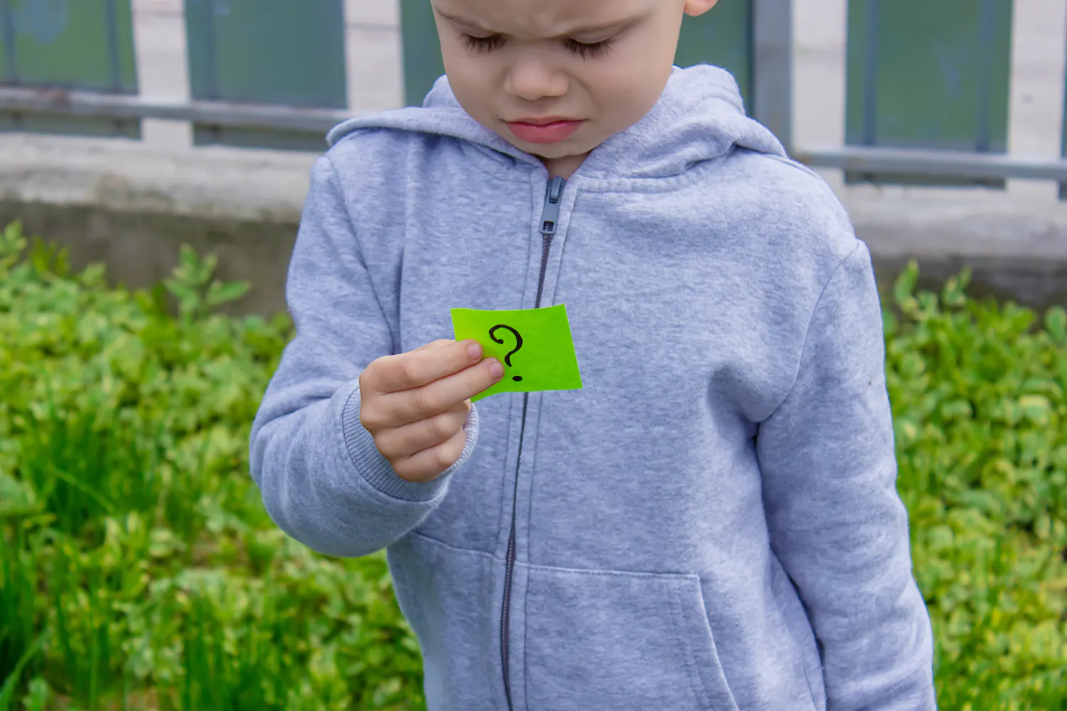 Enfant tenant un post-it qui se pose une question.