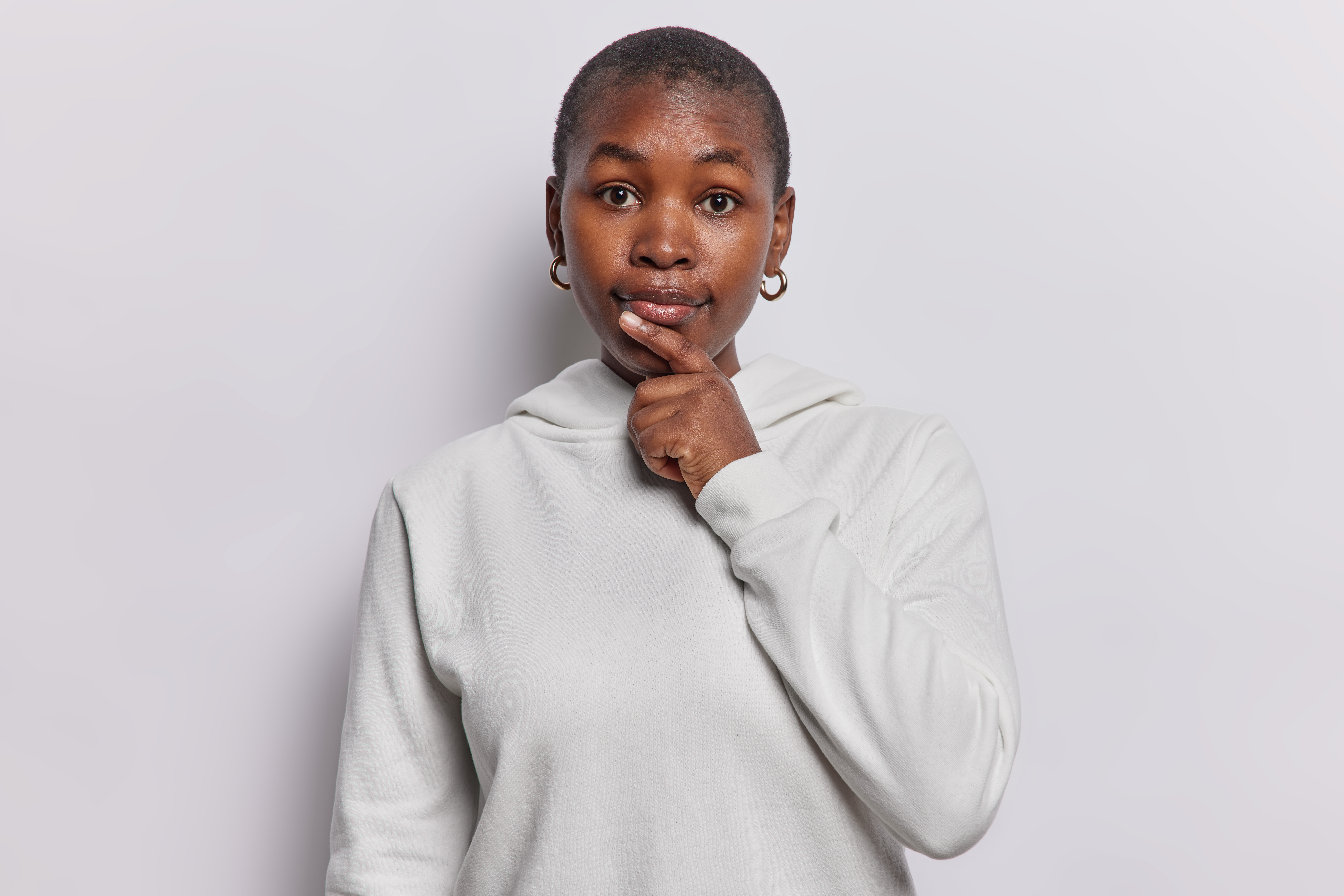 Femme se tenant le menton en se questionnant sur fond gris.