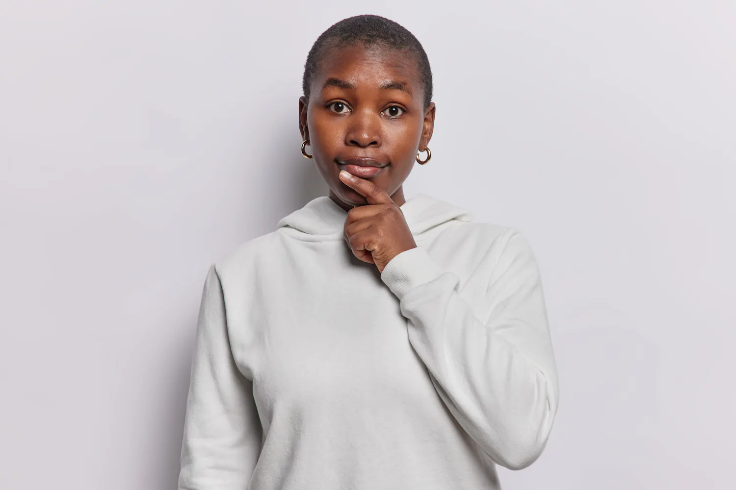 Femme habillée en gros se tenant le menton en se posant une question sur fond gris.