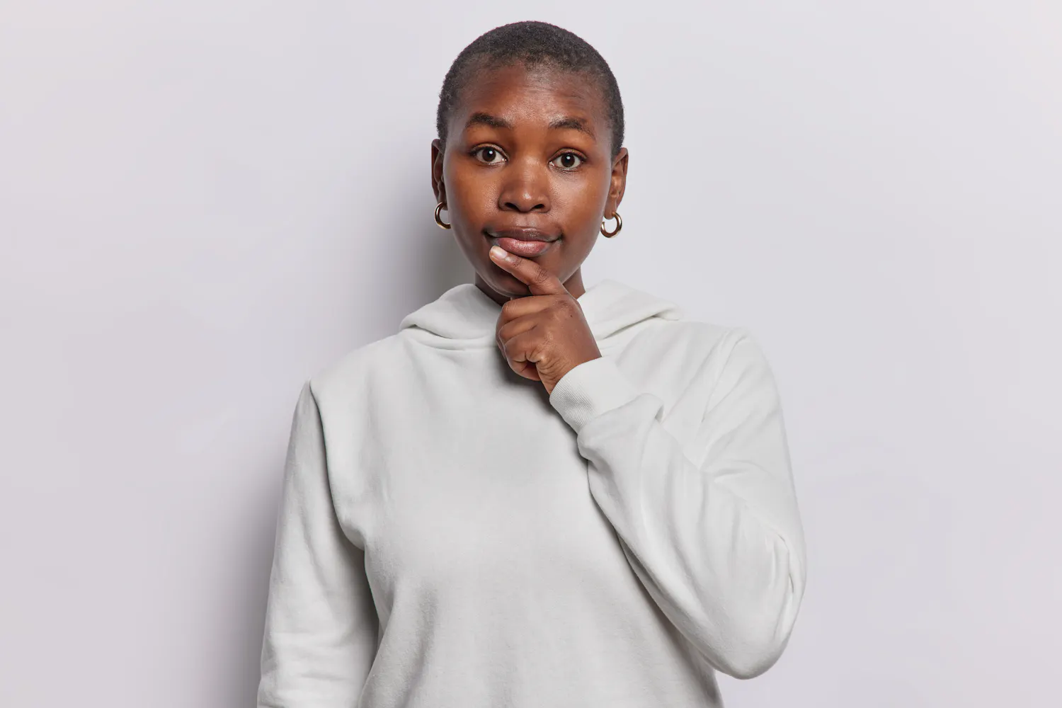 Femme habillée en gris se posant une question en se tenant le menton sur fond gris.