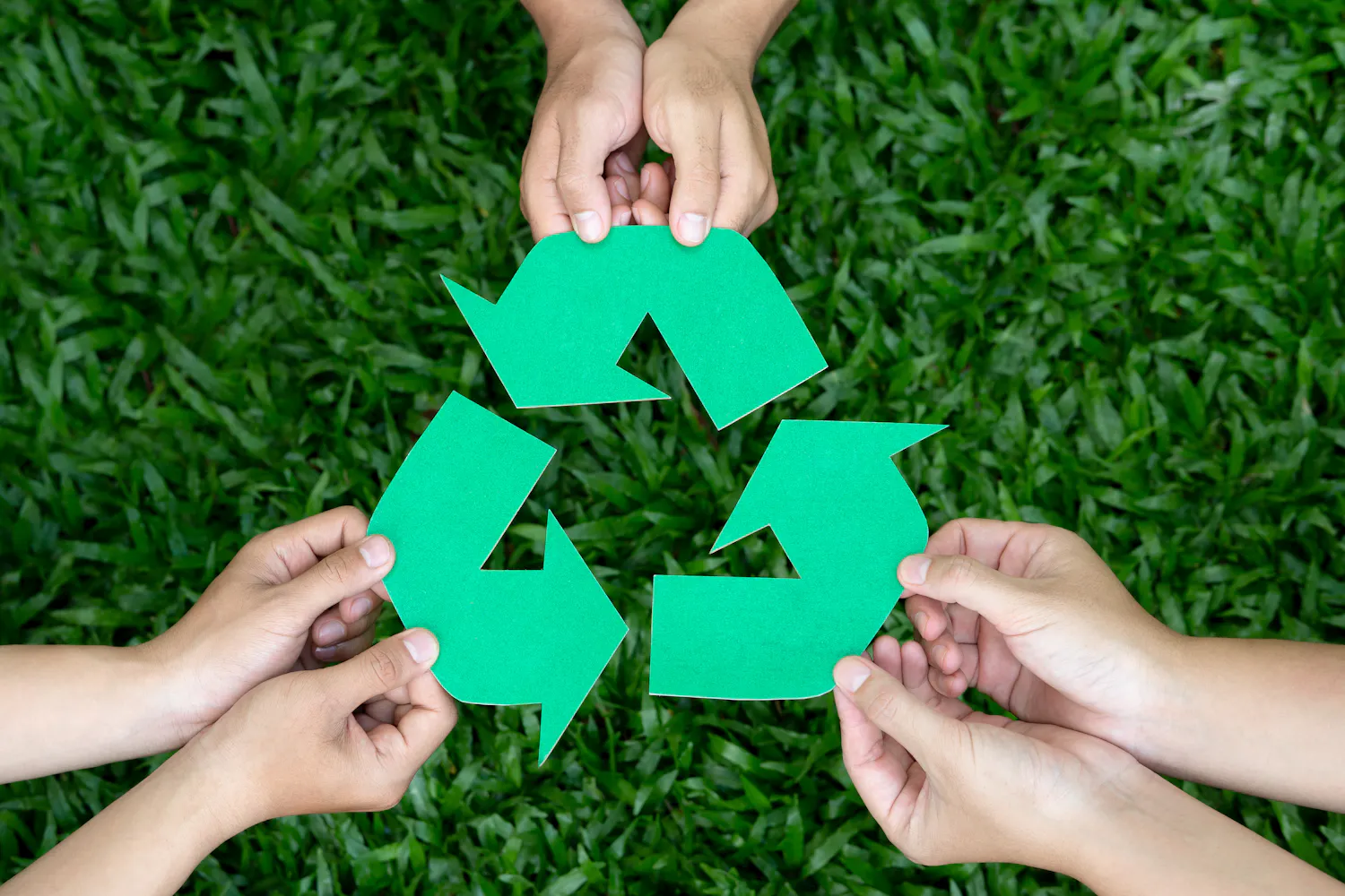 Logo recyclage tenu par six mains au dessus de l'herbe.