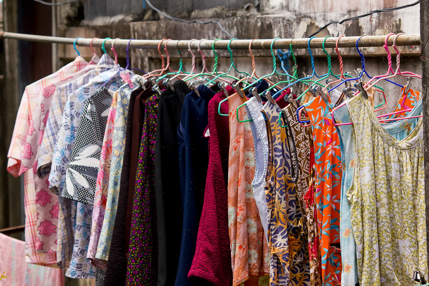 Vêtements divers colorés, sur des cintres et sur un vestiaire.