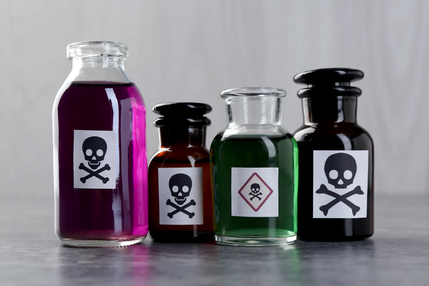 Quatre flacons colorés de produits dangereux avec des étiquettes tête de mort.
