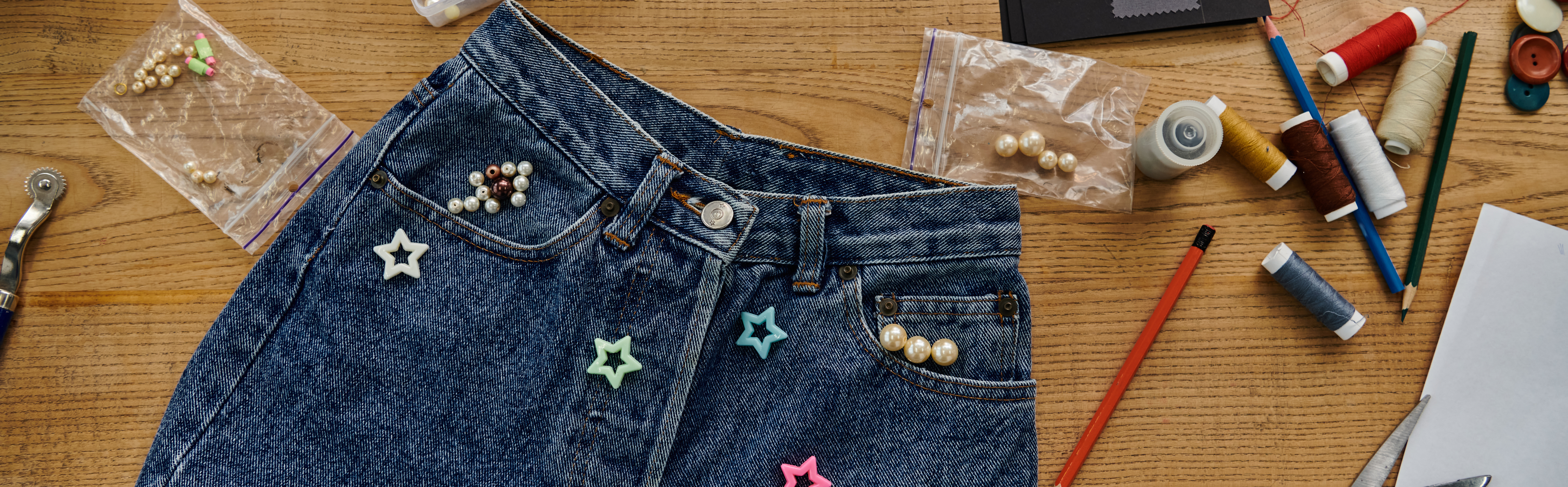 Jean customisé avec des perles de différentes formes et couleurs sur une table.