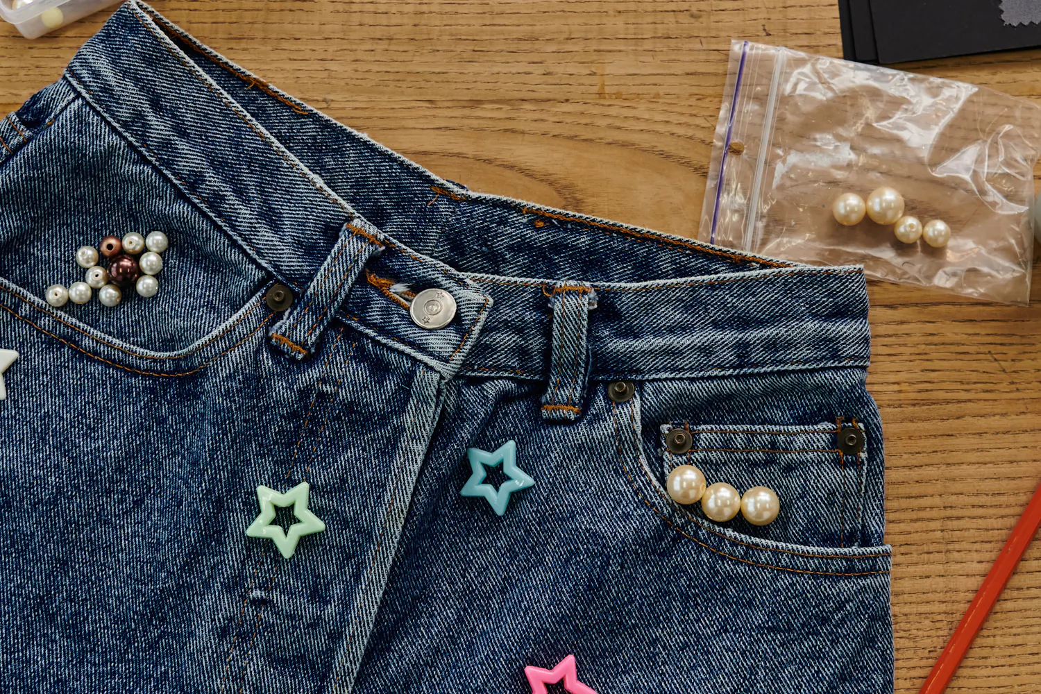 Jean customisé avec des perles de différentes formes et couleurs sur une table.