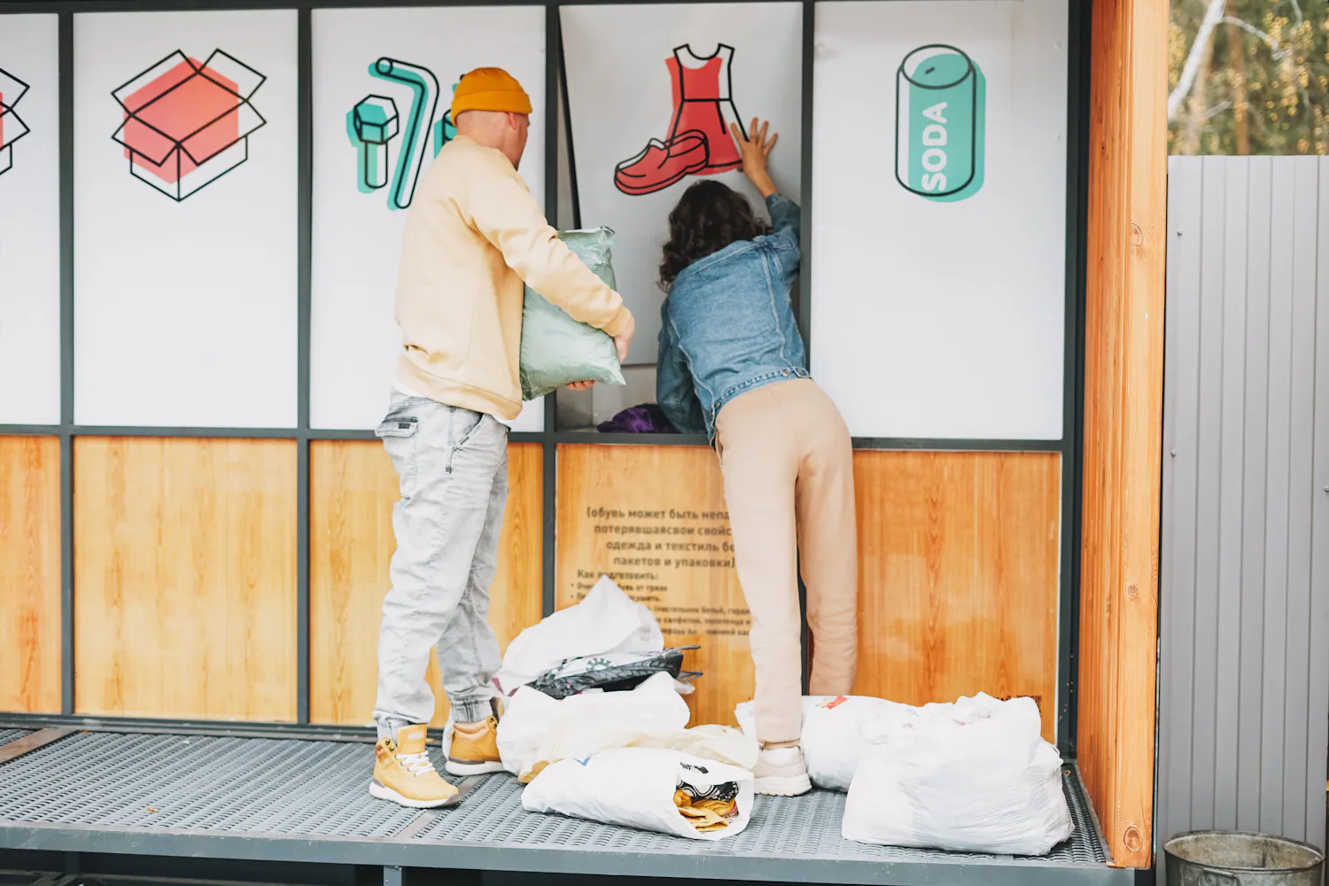 Bornes de recyclage dont une de vêtements, deux personnes y laissent des vêtements.