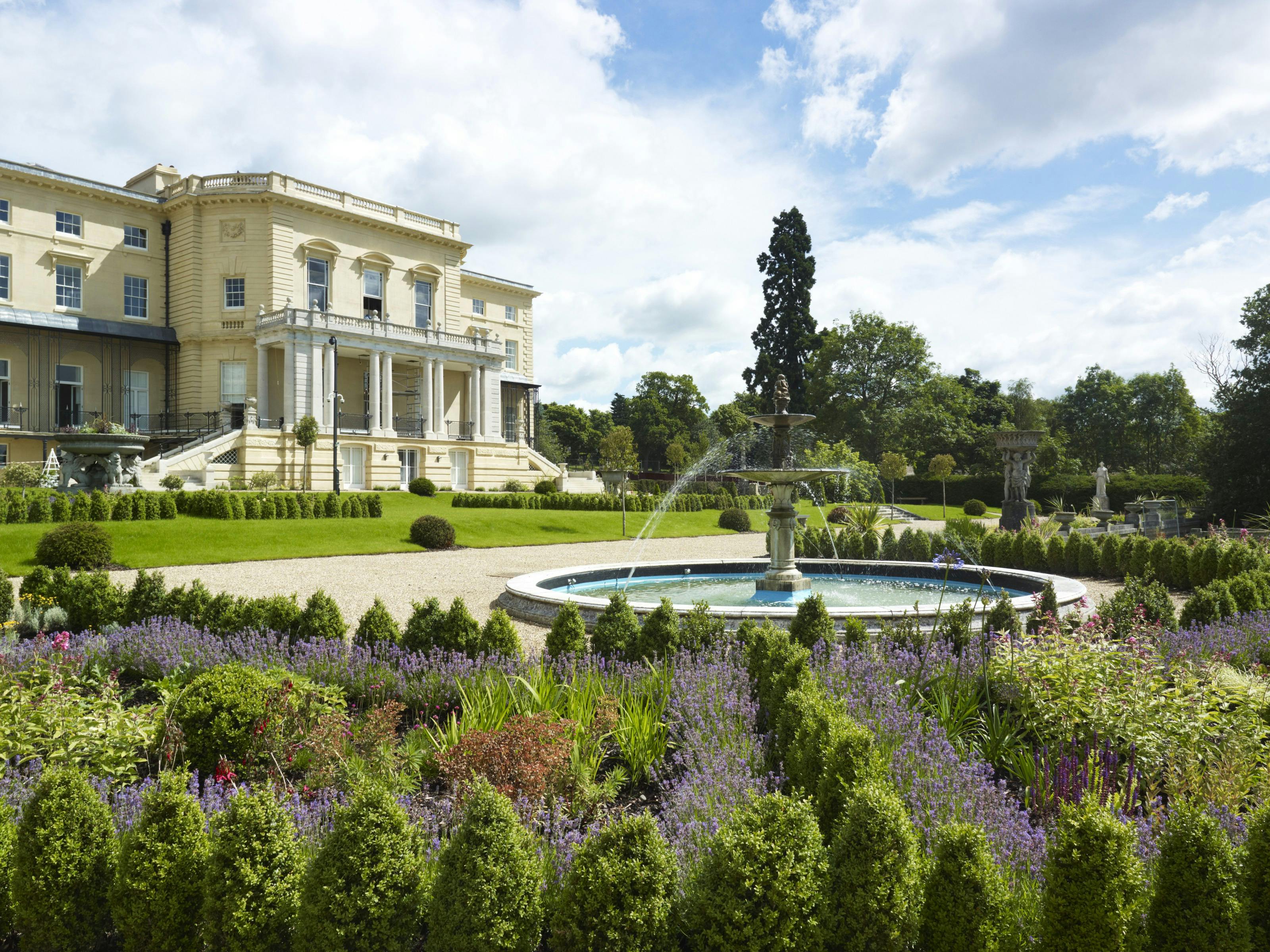 Caption: a large house with a fountain in the middle of a garden